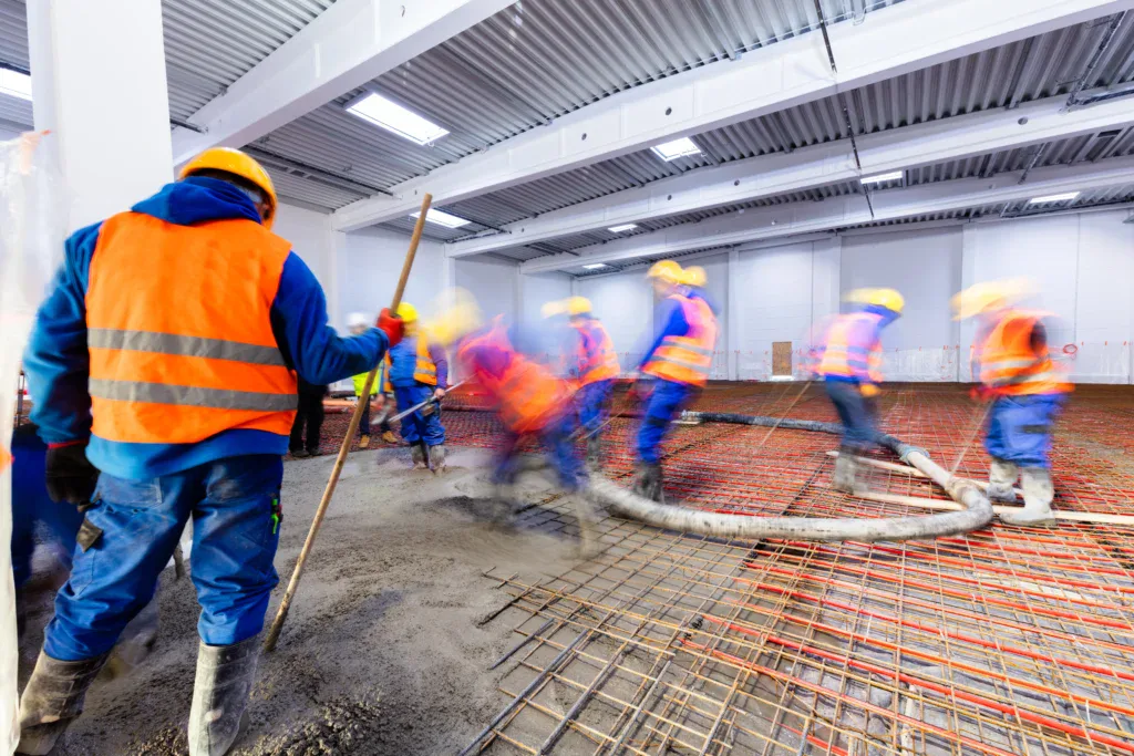 Construction workers pouring concrete on a floor with radiant heating pipes