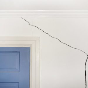Large, dark crack on a white wall above a blue door.
