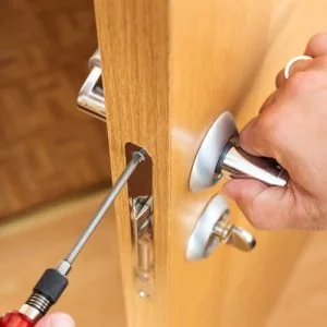 Hand using a screwdriver to fix a door handle on a wooden door.