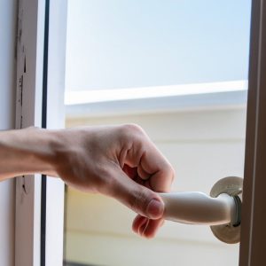 A hand opening a white door handle, with a bright outdoor view.