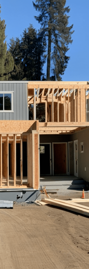 A modern house under construction with gray siding and exposed wood framing.