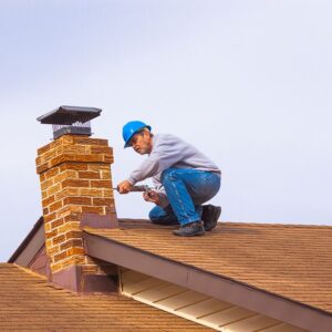 Man in blue hard hat working on a brick chimney on a brown roof