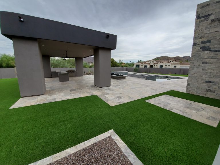 Stylish backyard landscape featuring a covered patio, fire pit, and swimming pool with lush green artificial turf.