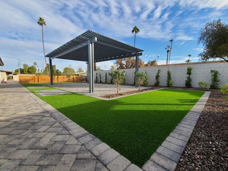 Bright artificial turf and paved patio with shade structure create inviting outdoor space.