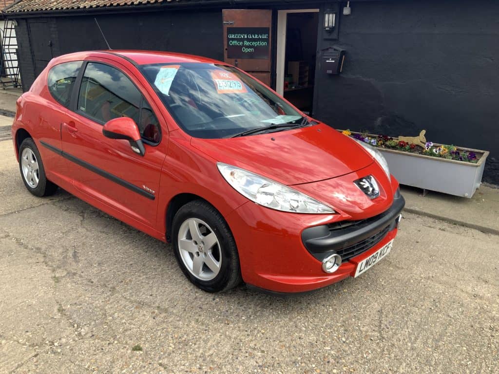 Red Peugeot 207 hatchback parked outside Greens Garage Suffolk.