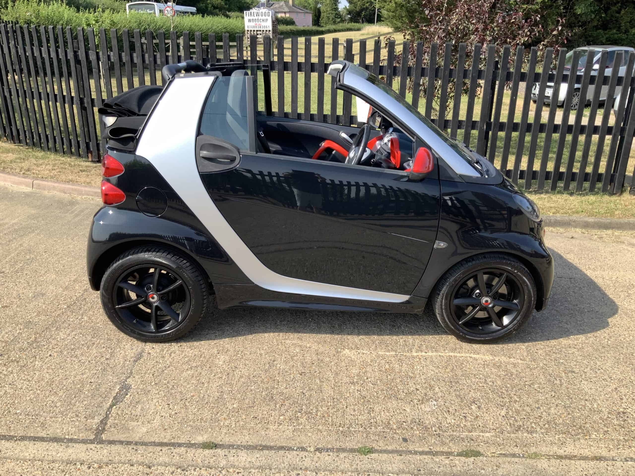 Black Smart ForTwo convertible with red interior, parked outdoors in Suffolk.