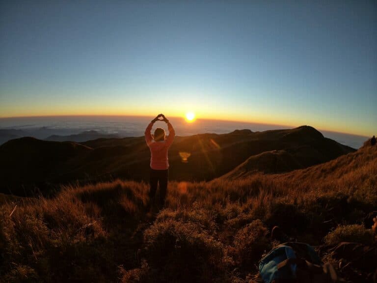 A person taking a photo with the sun rising on the horizon of Mount Pulag in Benguet