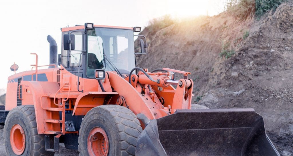 Orange front-end loader with a large bucket on a dirt construction site.