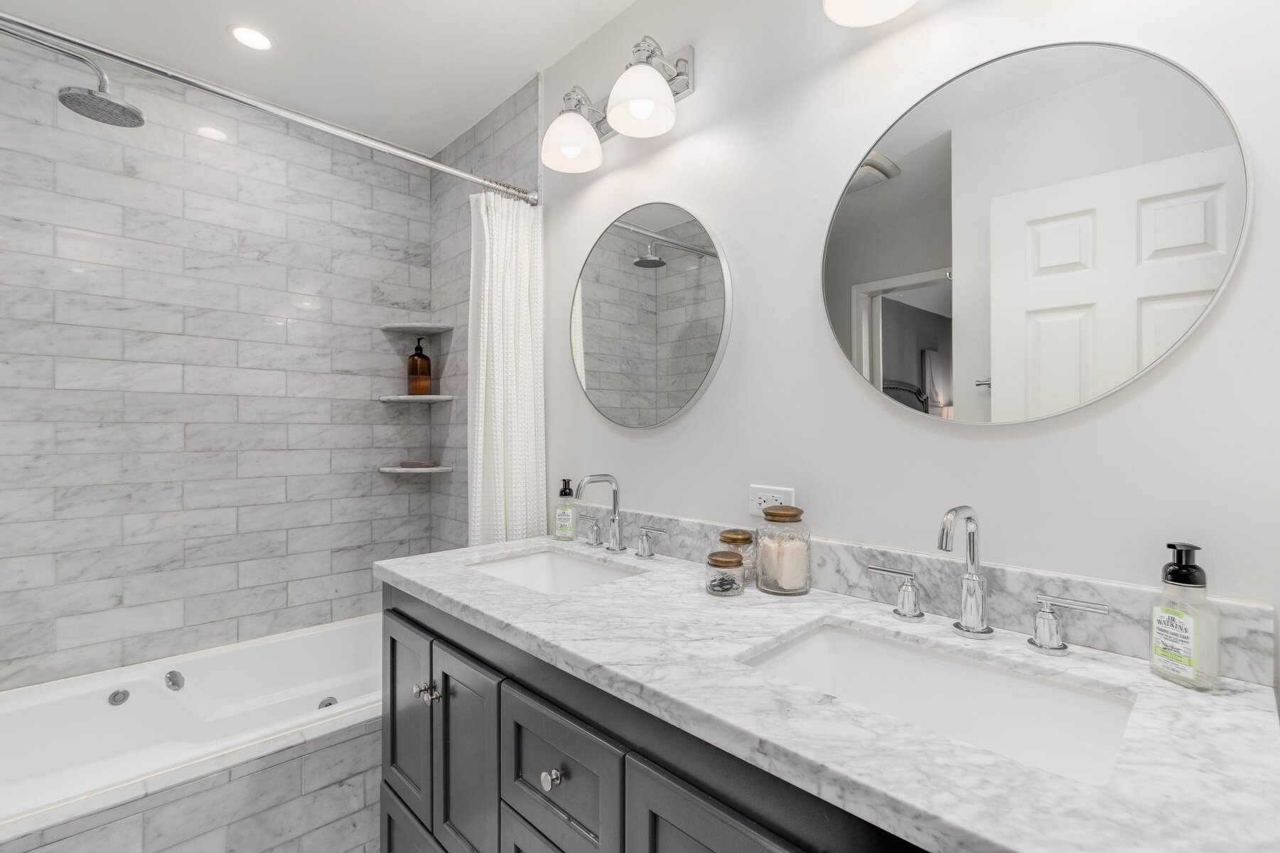 Modern bathroom with double vanity, marble tiles, and a bathtub with a shower.