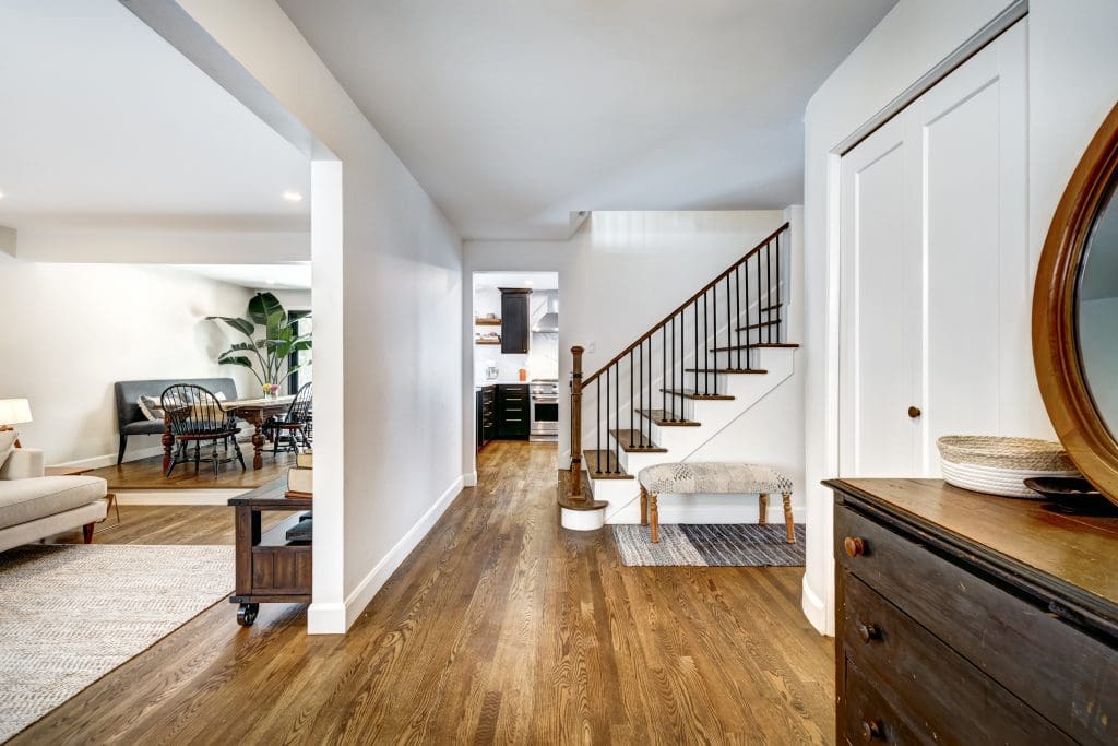 A home interior with wooden floors, a staircase, and a glimpse of a living area.