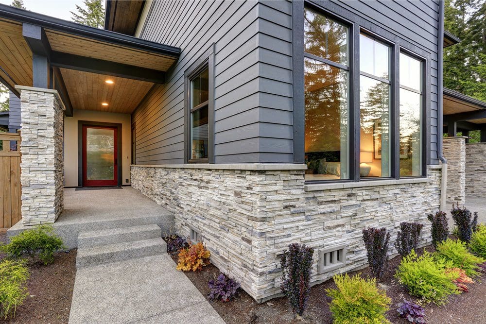Modern house exterior with dark gray siding, stone accents, and large windows.