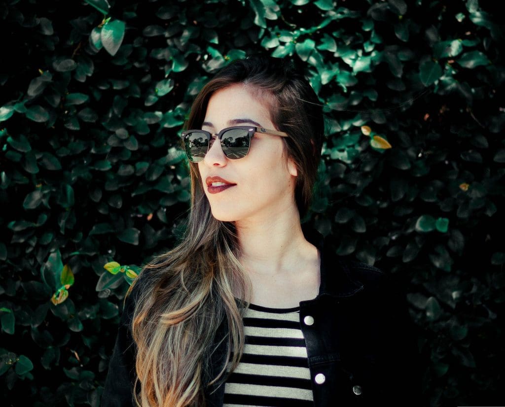 Woman with sunglasses and striped shirt against a green leafy background