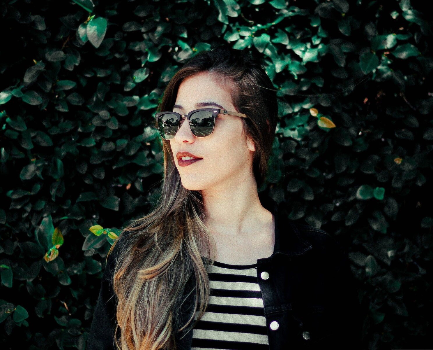 Woman with sunglasses and striped shirt against a green leafy background