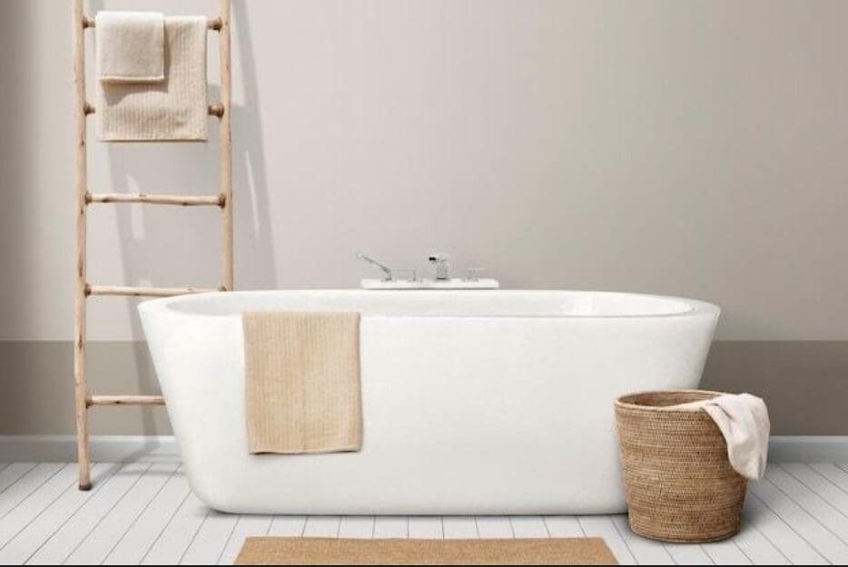 White freestanding bathtub in a minimalist bathroom with a wooden ladder and basket.