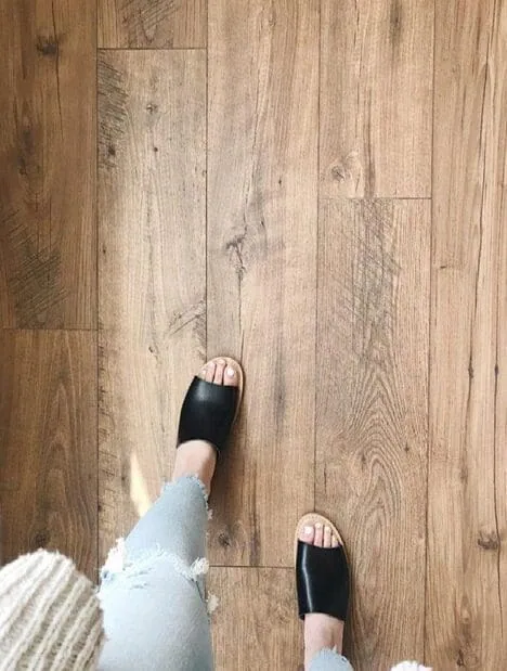 Person wearing black sandals and ripped jeans standing on a wooden floor.