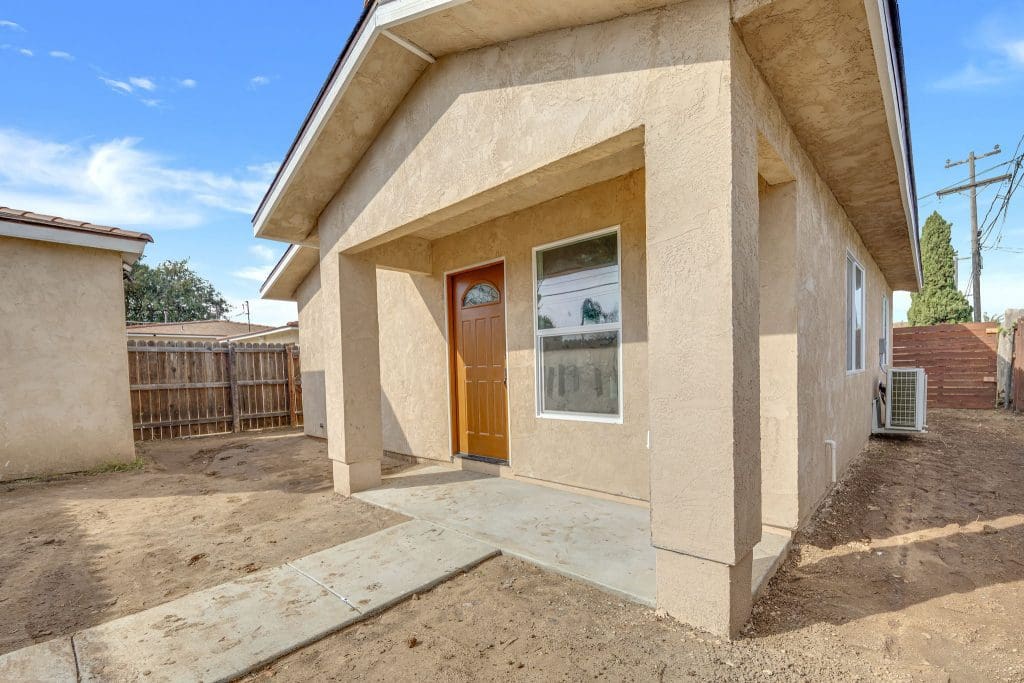 Front view of a small, tan stucco house with a brown door.