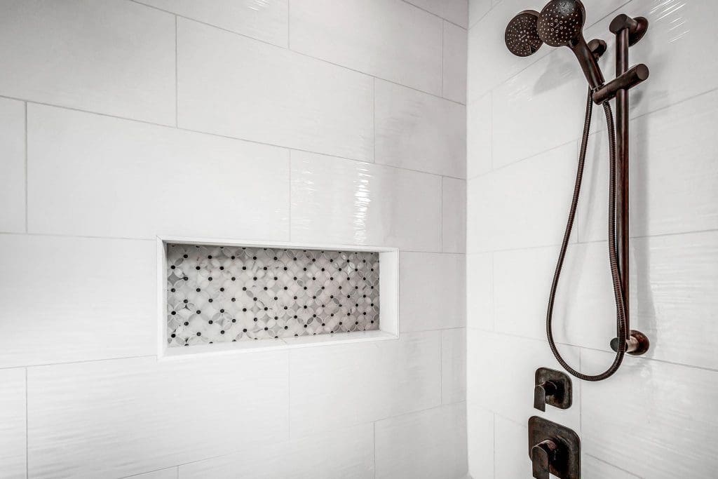 Modern white tiled shower with a decorative niche and dark bronze showerhead.