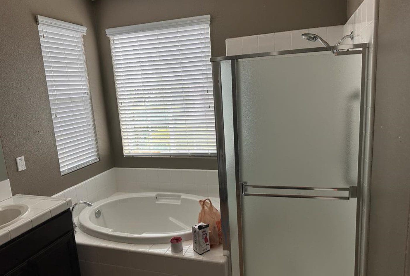 Bathroom with white bathtub, shower, and two windows with blinds.