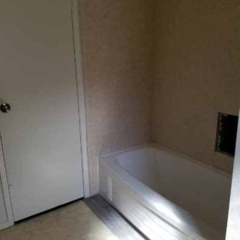 Empty white bathtub next to a closed white door in a room with light brown walls.