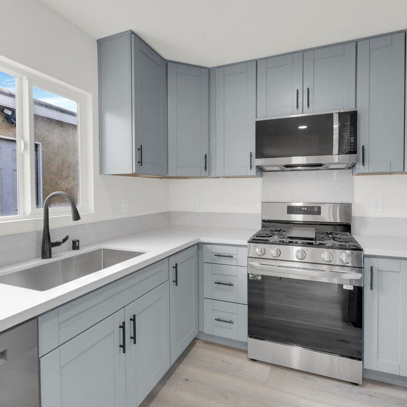 Modern kitchen with light gray cabinets, stainless steel appliances, and a sink.
