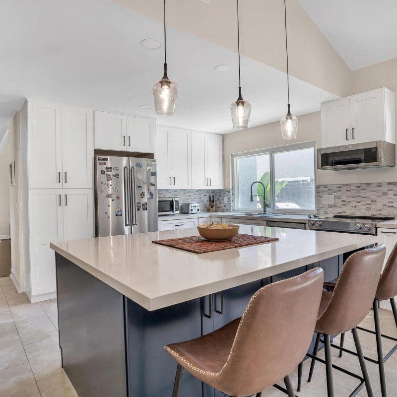 Modern kitchen with white cabinets, dark island, and three pendant lights.