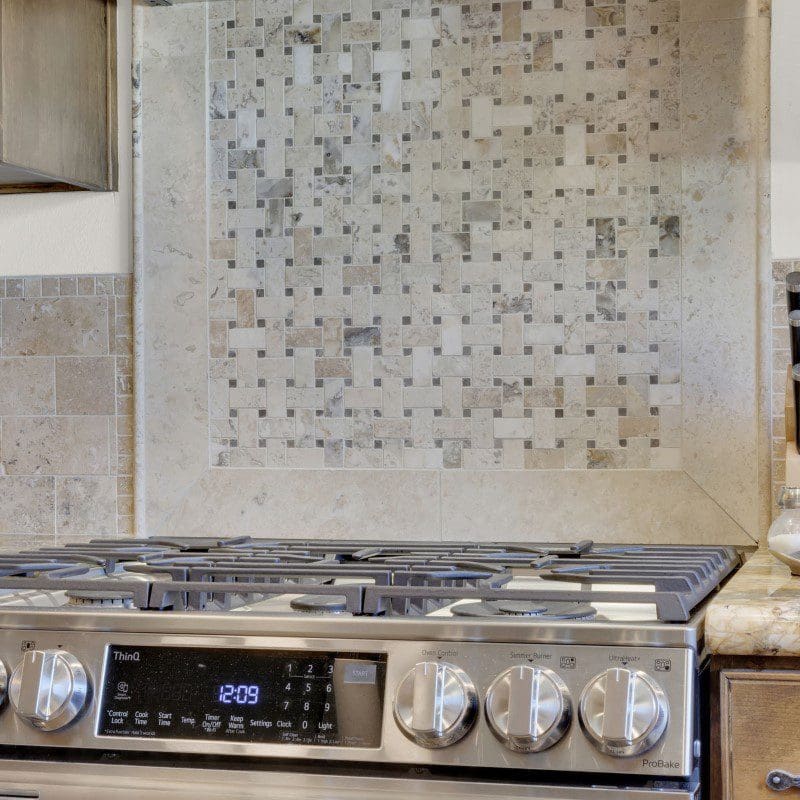 Close-up of a stainless steel gas range with a tiled backsplash.