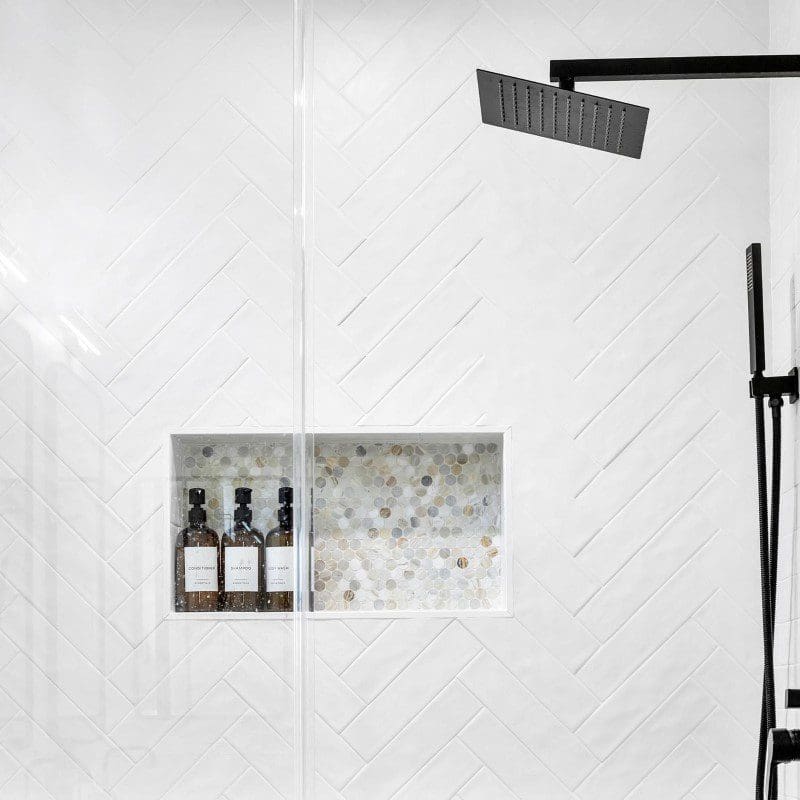Modern shower with white herringbone tiles and black fixtures.