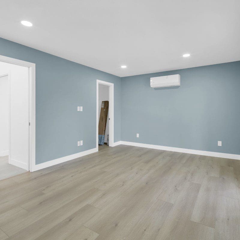 Empty room with light blue walls, white trim, and light wood flooring.