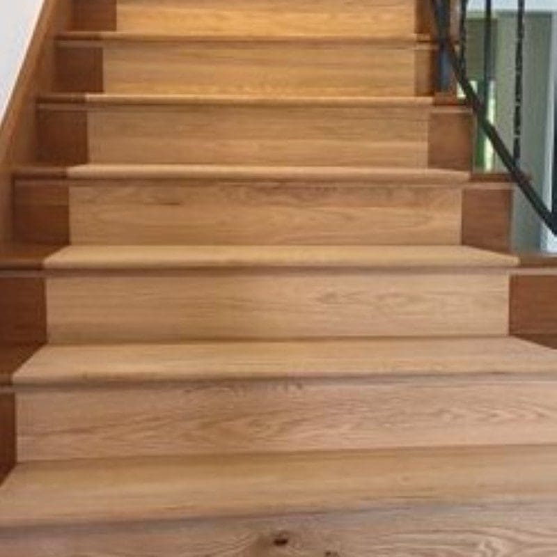Close-up of wooden stairs with a black metal railing.