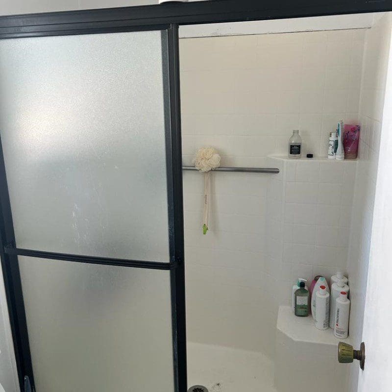 Shower with frosted glass door, white tiles, and various toiletries.