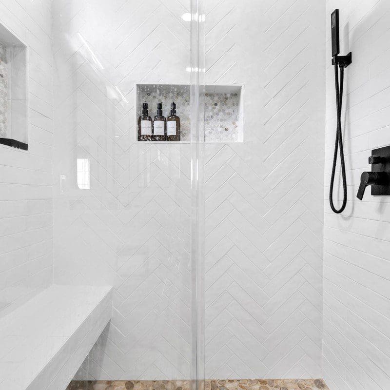 Modern white tiled shower with black fixtures and built-in shelves