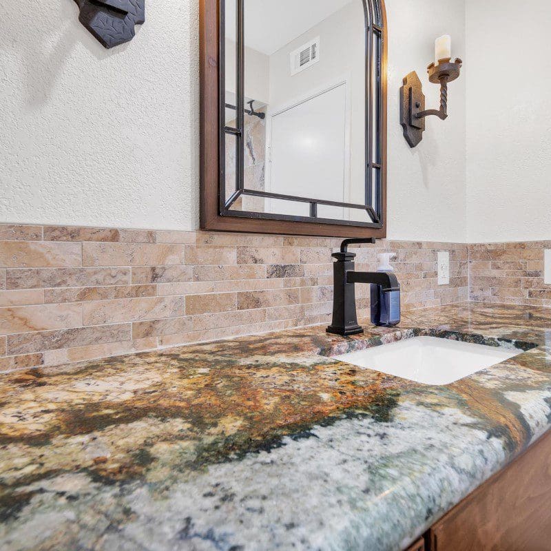 Bathroom vanity with granite countertop, dark faucet, and decorative mirror