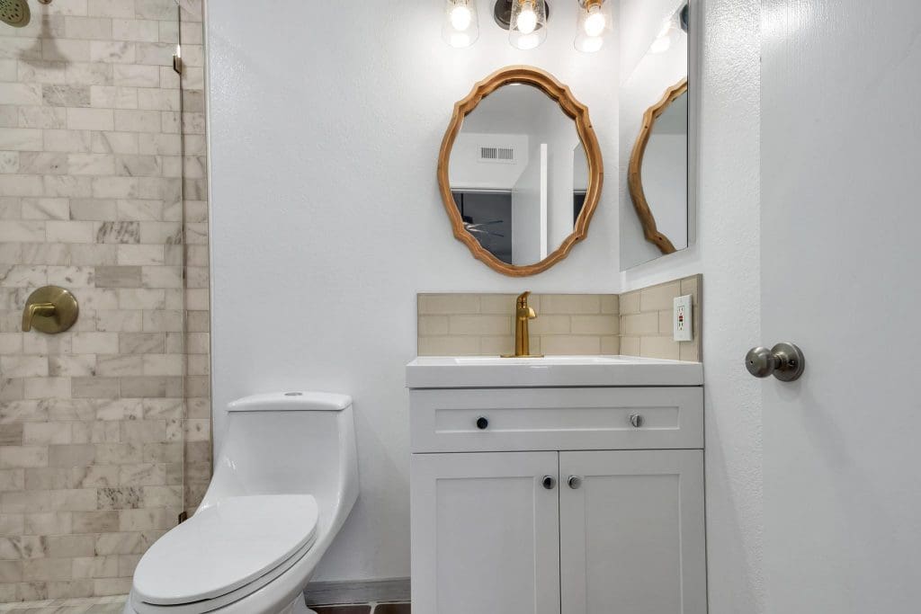 Bathroom with white vanity, gold faucet, oval mirror, and tiled shower.