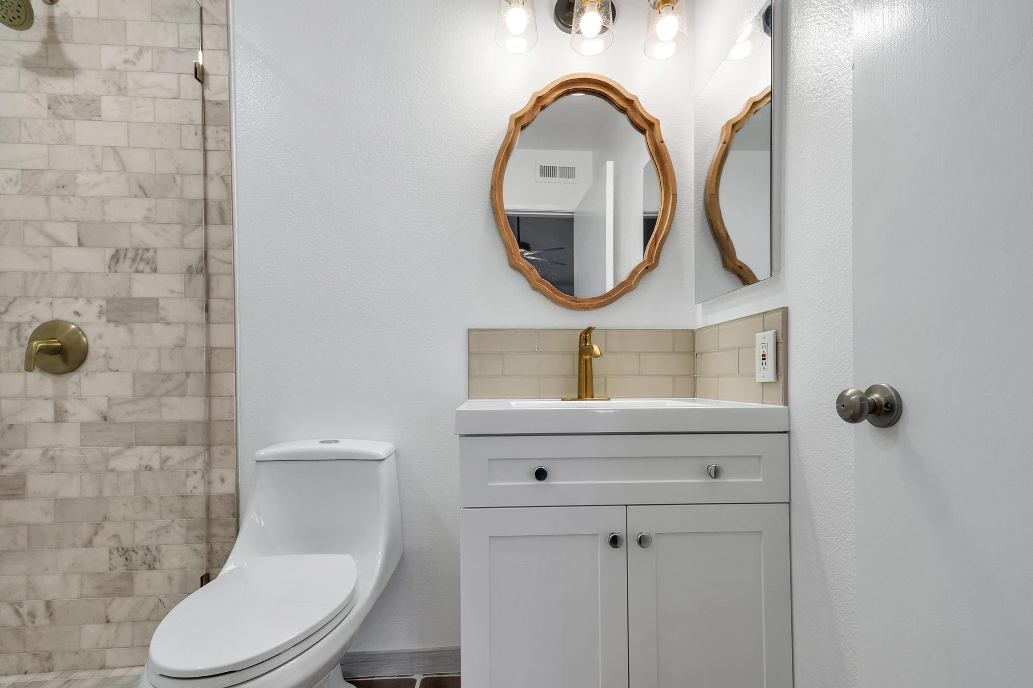Bathroom with white vanity, gold faucet, oval mirror, and tiled shower.