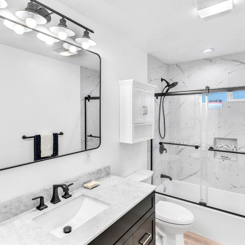 Modern bathroom with white marble tiles, black fixtures, and a glass shower.