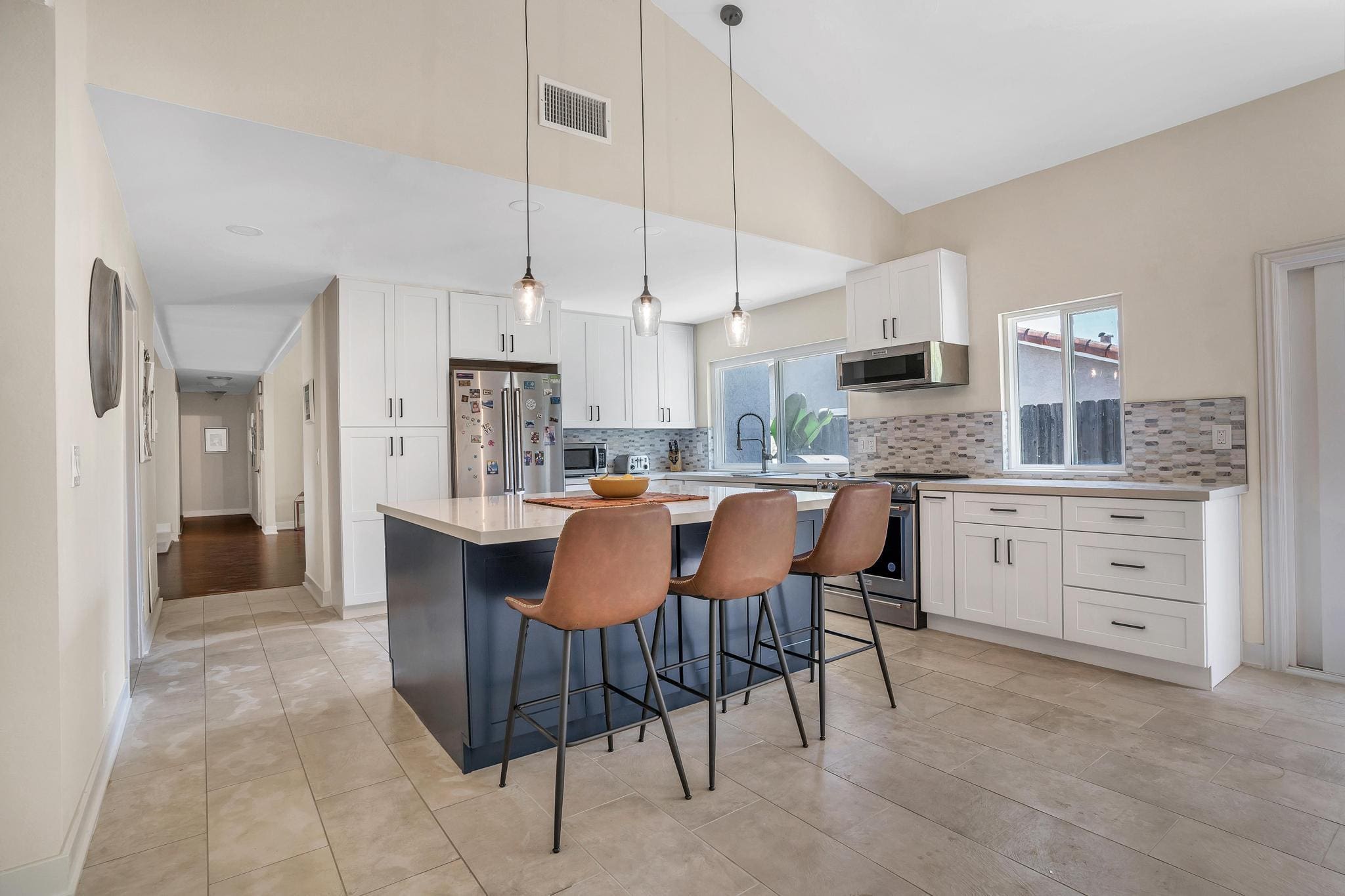 Modern kitchen with a dark blue island and three brown bar stools.