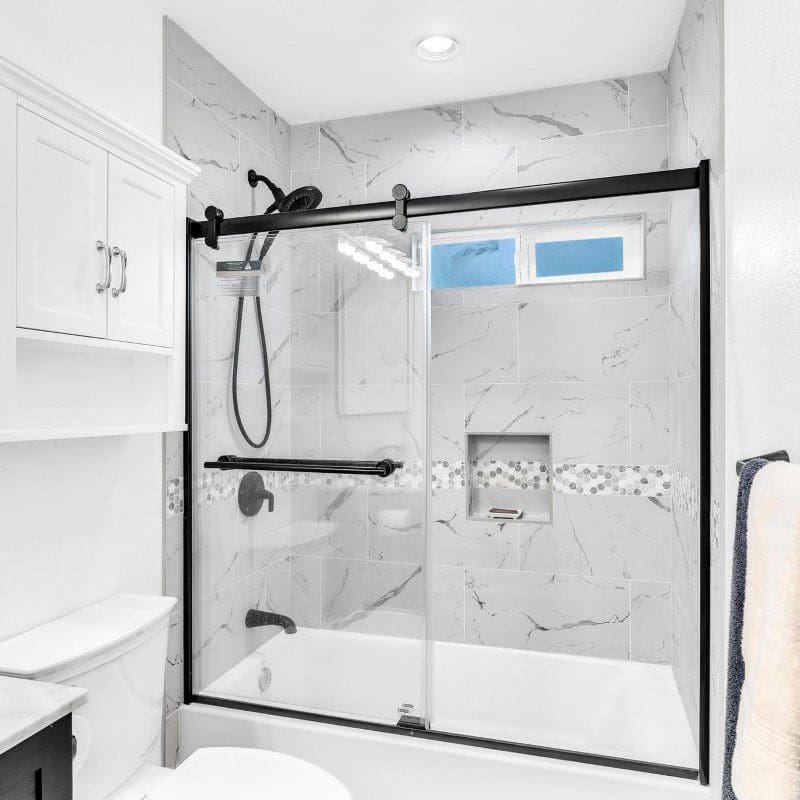 Modern bathroom with white marble tile shower and black framed glass door.