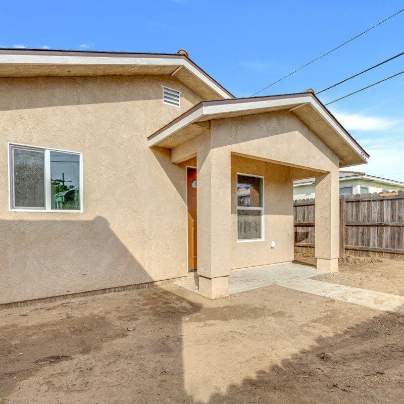 Front view of a small, light brown stucco house with a porch.