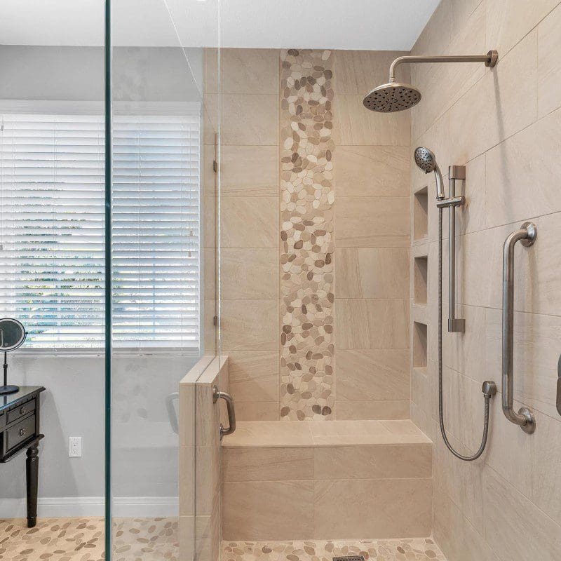 Modern bathroom shower with beige tiles, pebble accents, and glass enclosure.