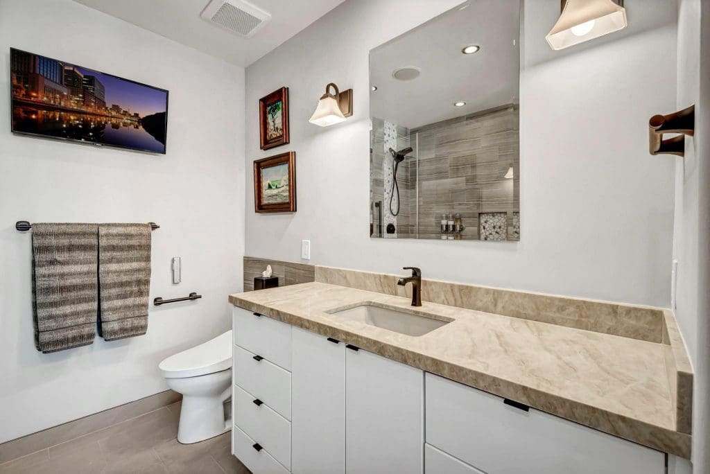 Modern bathroom with a large vanity, toilet, and wall-mounted TV.