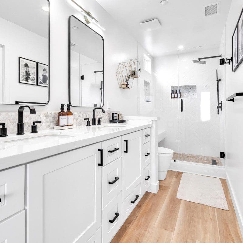 Modern white bathroom with double vanity, black fixtures, and glass shower.
