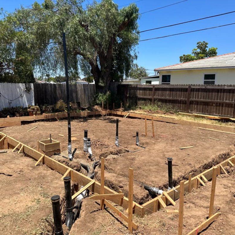 Foundation framing and plumbing pipes in a dirt construction site.