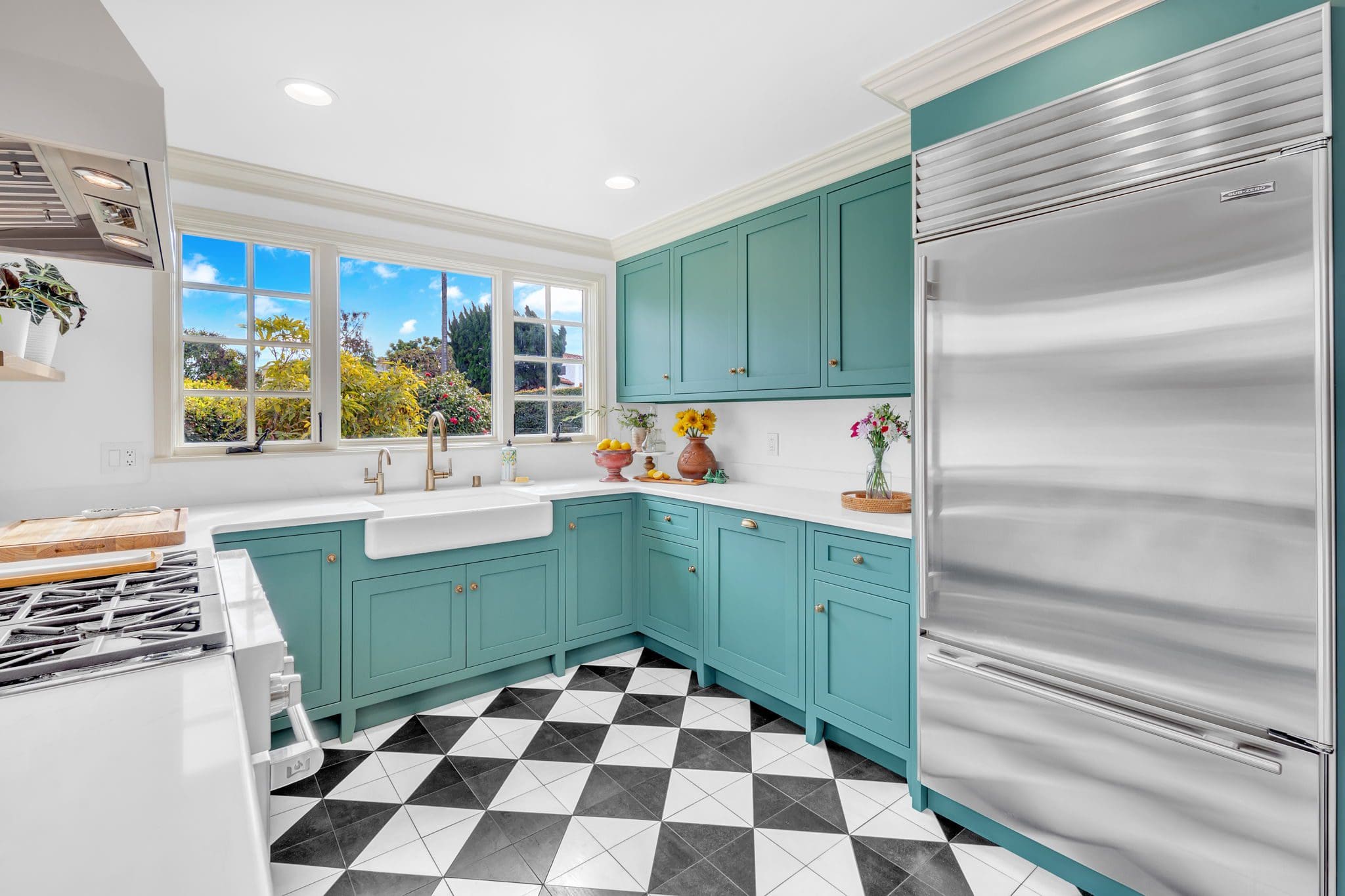 Bright kitchen with teal cabinets, white countertops, and checkerboard floor.
