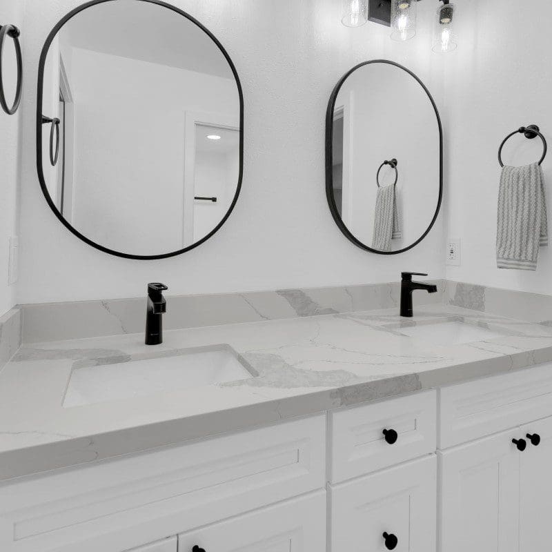Double vanity with oval mirrors, black faucets, and white marble countertop.