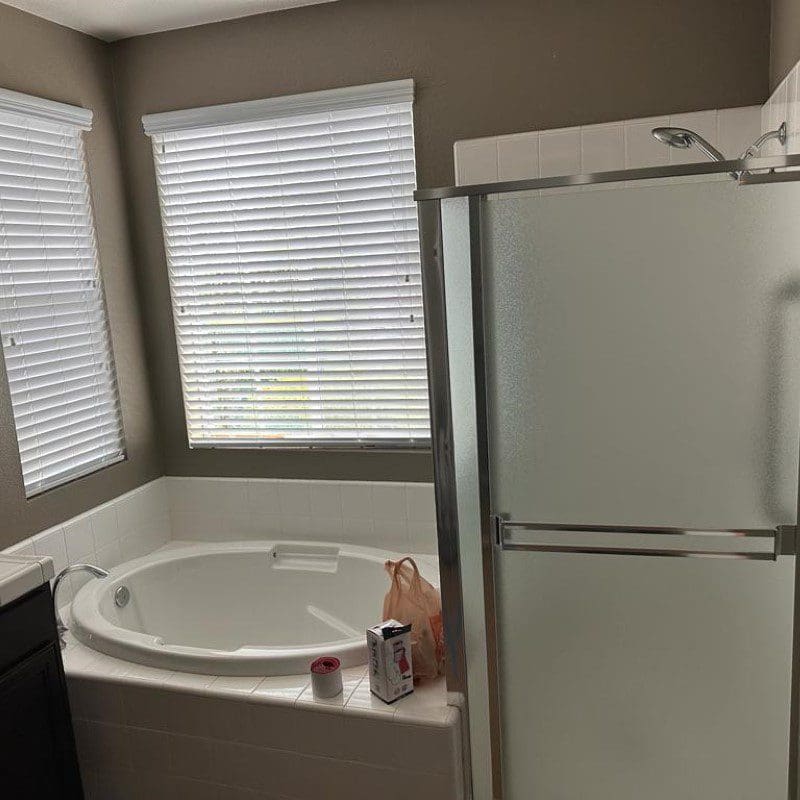 Bathroom with a white bathtub, two windows, and a shower stall.