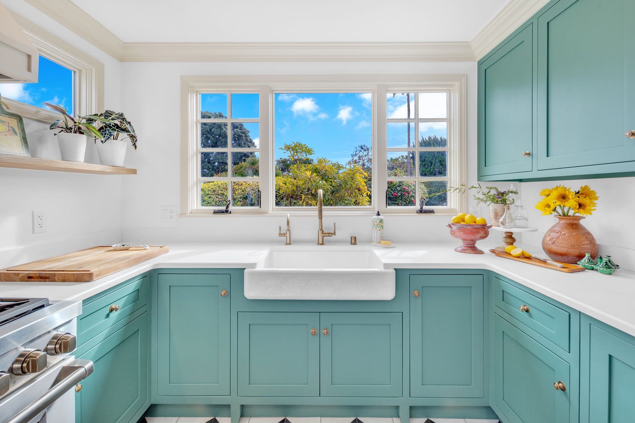 Bright kitchen with teal cabinets, white countertops, and a large window.
