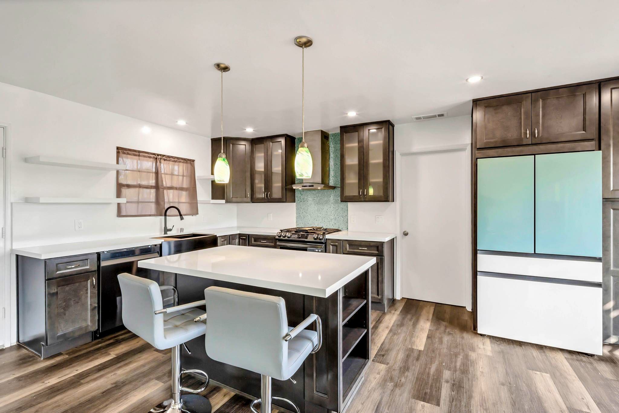Modern kitchen with dark cabinets, white island, and light green pendant lights.