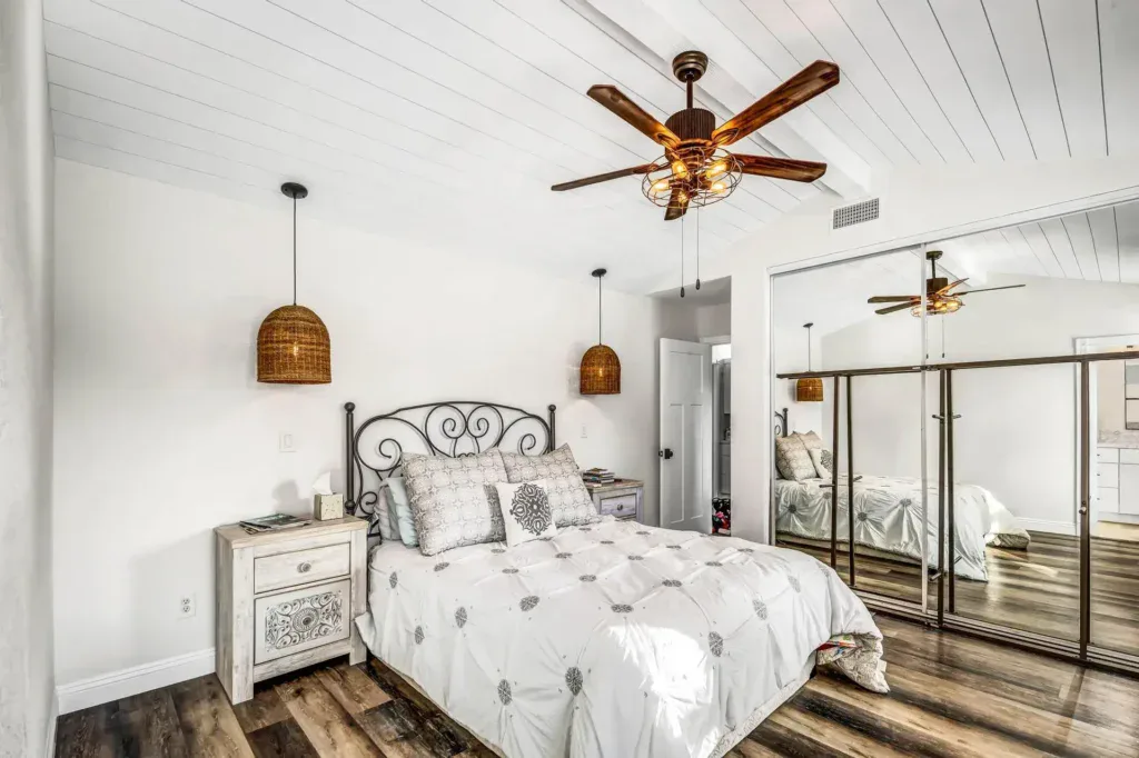 Bedroom with white walls, wooden floor, and a bed with decorative headboard.
