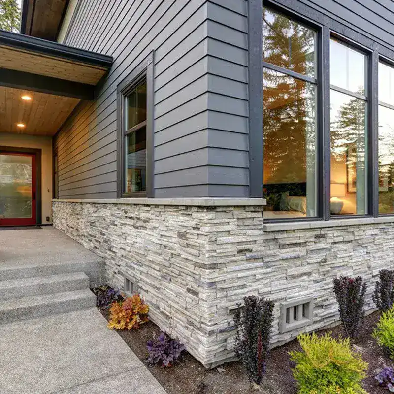 Modern house exterior with gray siding, stone foundation, and large windows
