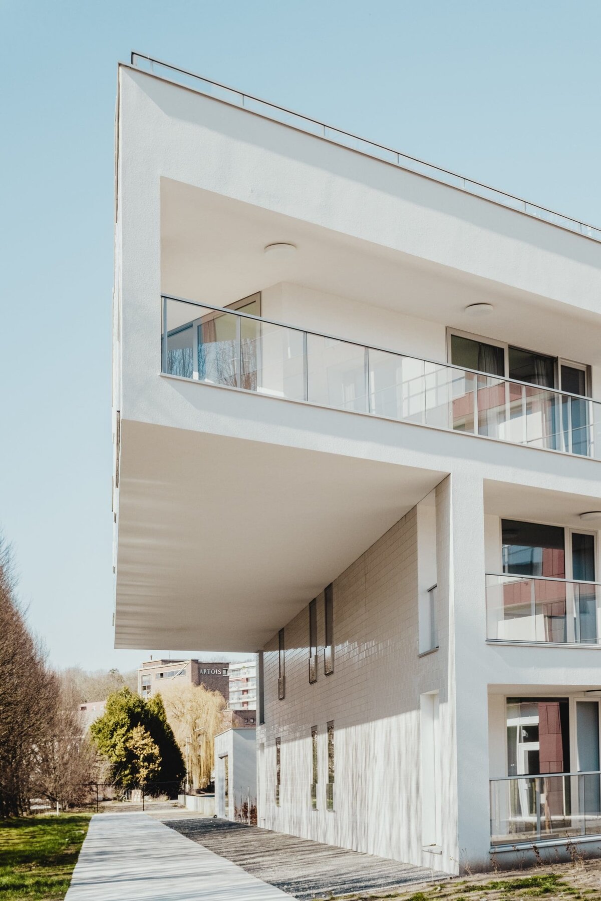 Modern white building with balconies and glass railings under a clear sky.